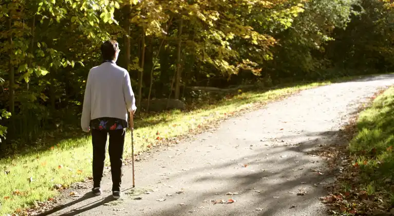 Senior woman, using a cane, walking on a path through a wooded area